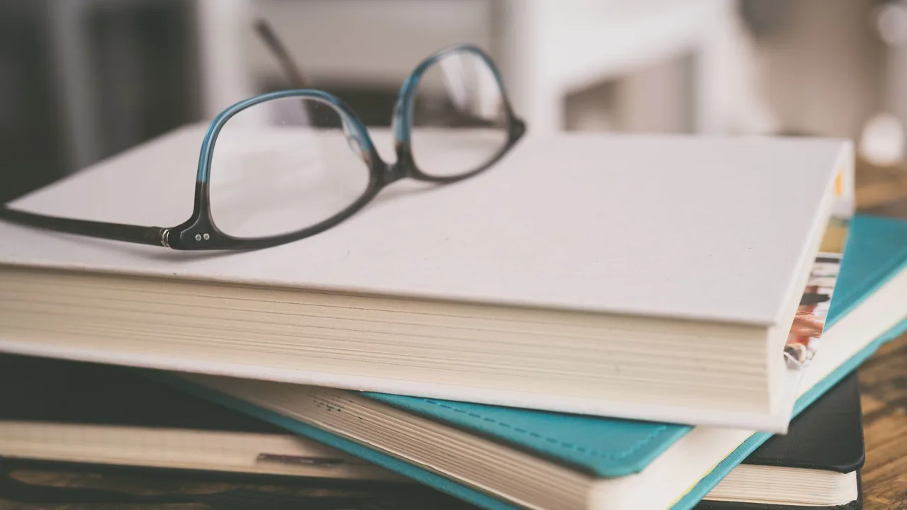 A stack of study books with eyeglasses on a desk.